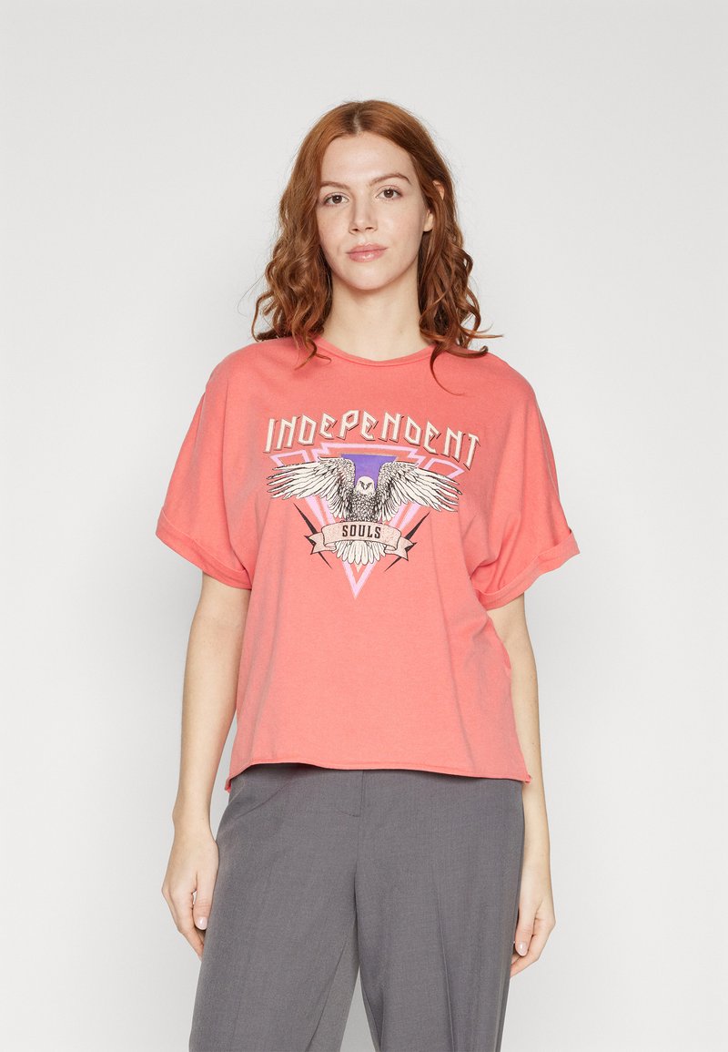 Coral oversized t-shirt made of soft fabric featuring a graphic design of an eagle with the text "Independent Souls." Short sleeves.