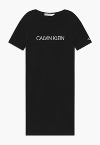 Černé bavlněné tričko s krátkým rukávem a kulatým výstřihem. Na přední straně je bílý text "CALVIN KLEIN" a na rukávu je malé logo.