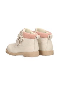 Botas de tobillo beige con forro de fieltro rosa, correa de velcro y suela de goma texturizada. Presentan un detalle de estrella y un acabado de cuero suave.