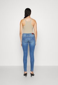 Vaqueros pitillo azules de talle alto, con cuatro bolsillos y una parche de cuero marrón. Combinados con una camiseta sin mangas beige y tacones negros.