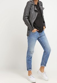 Giubbotto di pelle nera da biker sopra un top nero, abbinato a jeans chiari strappati e sneakers bianche. Polsini arrotolati in vista.