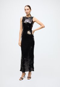 Black sequin evening gown with a fitted silhouette, sleeveless design, and floor-length hem. Paired with black strappy heels.