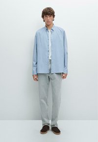 Hellblaues Hemd mit Knopfleiste, lange Ärmel, lässige Passform, kombiniert mit hellgrauen Jeans und dunkelbraunen Schuhen. Einfaches Design ohne Muster.