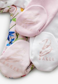 Tri páry detských ponožiek: jeden biely a dva ružové s logom "BAKER". Na látke je viditeľný kvetinový vzor. Mäkká bavlnená textúra.