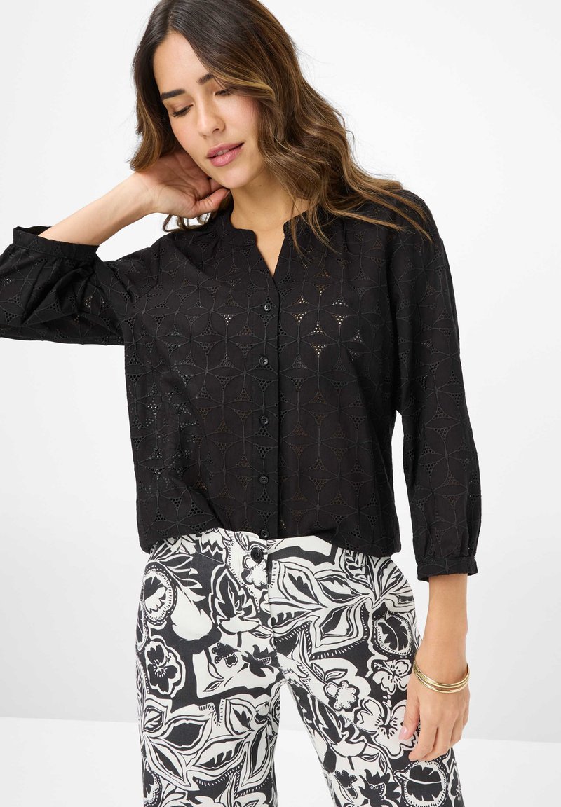 Blusa nera con bottoni, caratterizzata da un motivo testurizzato, con maniche a tre quarti e colletto alla mandarina. Abbinata a pantaloni a fantasia bianchi e neri.