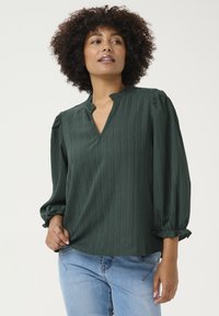 Blusa verde scuro con scollatura a V, tessuto testurizzato e maniche arricciate. Il design presenta una vestibilità rilassata e sottili righe verticali.
