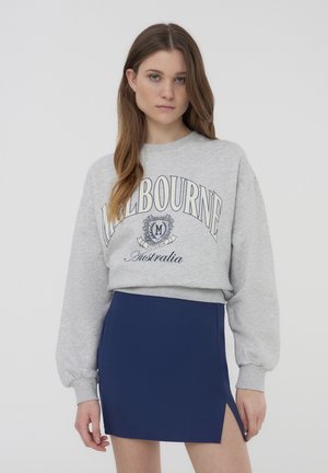 Felpa grigia con la scritta "MELBOURNE" e una minigonna blu navy con uno spacco laterale. Tessuto testurizzato, design casual, stile aderente.