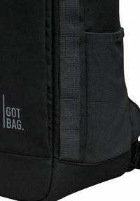 Mochila negra hecha de tejido texturizado, con un bolsillo lateral y correas ajustables. Logotipo de la marca "GOT BAG." impreso en blanco en el frente.