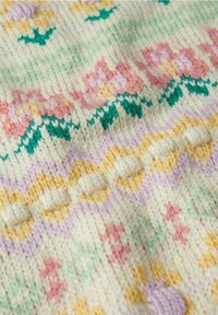 Couverture en tricot avec des motifs floraux pastel en rose, jaune et vert sur un fond crème, agrémentée d'accents en relief en forme de boules et d'un motif en zigzag.
