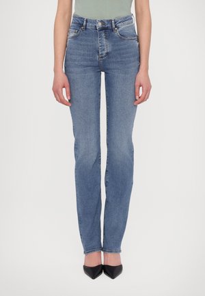Hochtaillierte blaue Jeans aus Denim mit geradem Bein, ausgestattet mit Fronttaschen und einem subtilen Ausbleichungseffekt. Getragen mit schwarzen spitzen Absätzen.