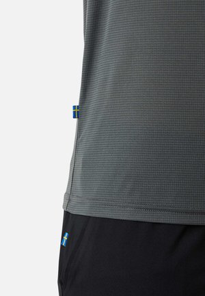 Das graue, strukturierte Hemd und die schwarze Hose haben beide kleine schwedische Fähnchenetiketten in der Nähe des Saums und der Taschenbereiche.