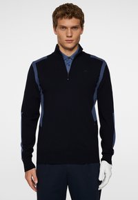 Marinblå tröja med kvartsgång krage, kontrasterande ljusblå sidopaneler, mjuk stickad textur och ribbstickade ärmslut. Stylerad med en skjorta med krage.