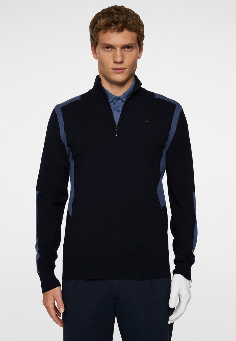 Marinblå tröja med kvartsgång krage, kontrasterande ljusblå sidopaneler, mjuk stickad textur och ribbstickade ärmslut. Stylerad med en skjorta med krage.