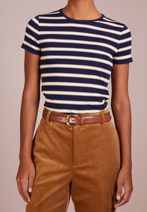 Personne portant une chemise à manches courtes rayée bleu marine et blanc rentrée dans un pantalon en velours côtelé marron taille haute avec une ceinture marron.