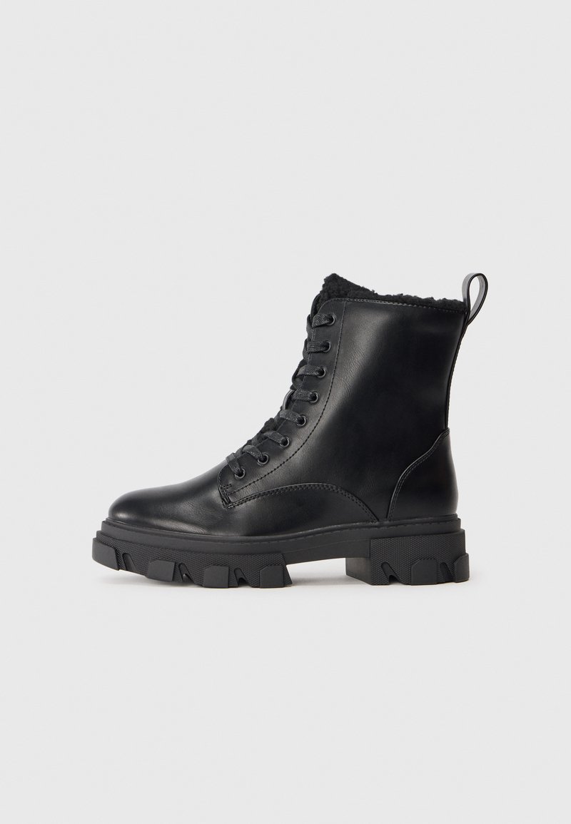 Bottines en cuir noir avec une semelle en caoutchouc épaisse, un système de laçage à l'avant et une douce fourrure à l'intérieur au niveau du col. Elles possèdent une languette à l'arrière pour un enfilage facile.