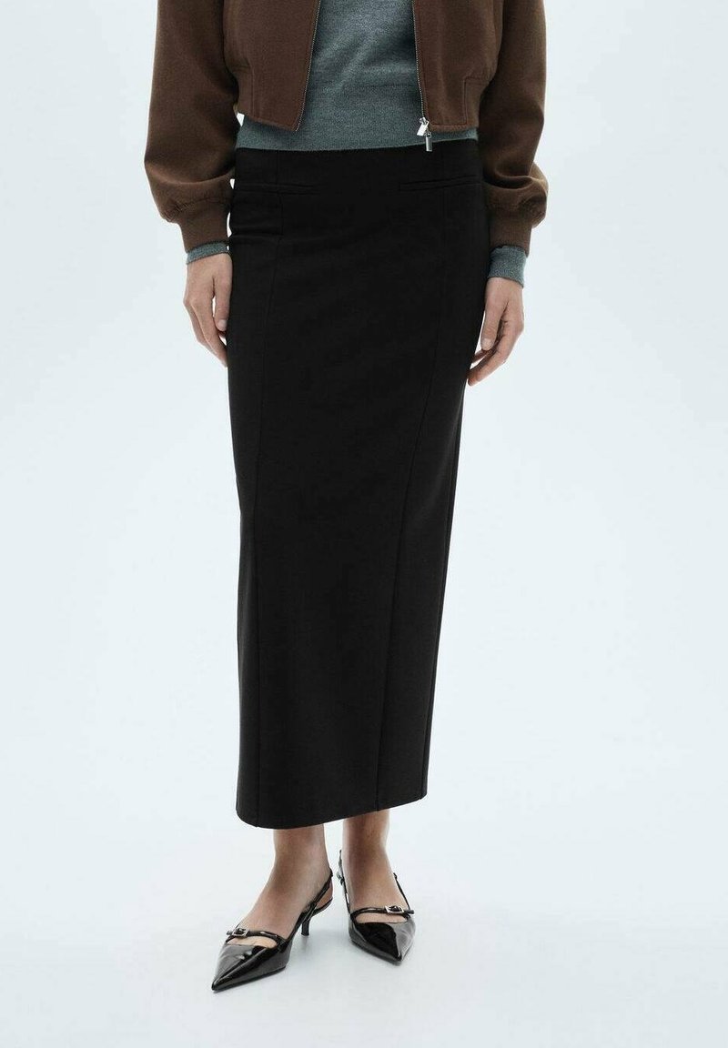 Femme portant une jupe midi noire taille haute, un haut gris, une veste zippée marron et des escarpins slingback noirs à bout pointu.