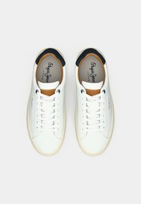 Baskets en cuir blanc avec un accent beige sur la languette, un col noir et des lacets blancs. Elles présentent une semelle texturée et un logo de marque imprimé.