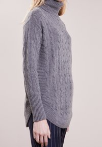 Suéter de cuello alto de punto gris con dobladillo acanalado y aberturas laterales, que presenta un patrón texturizado y material de lana suave.