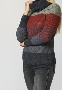 Pull en tricot à col roulé avec des rayures horizontales rouges, grises et gris foncé. Tissu texturé avec une coupe décontractée et des poignets côtelés.