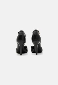 Black high-heeled shoes with a smooth leather texture, pointed toes, and a thin stiletto heel. Adjustable ankle strap with metal buckle.