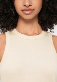 Beige ribbet tanktop med rund halsudskæring og brede stropper, der har en blød tekstur og minimale syninger.