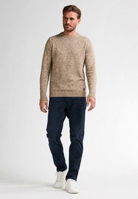 Pulover bej tricotat, cu guler rotund, asortat cu blugi albastru închis și adidași albi. Prezintă un material texturat și manșete bufante.