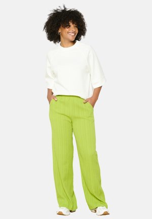 Weißer übergroßer Sweatshirt kombiniert mit strukturierten, leuchtend grünen, weiten Hosen, die einen elastischen Bund und Seitentaschen haben.