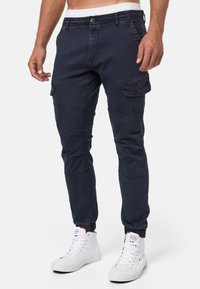 Pantalones cargo azul marino, con múltiples bolsillos laterales, puños elásticos y cierre de botón. Fabricados con una resistente mezcla de algodón.