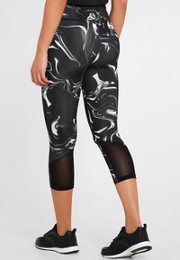 Leggings a marmorizzazione bianca e nera con inserti in rete, tessuto elasticizzato e taglio a metà polpaccio, abbinati a scarpe da ginnastica nere.