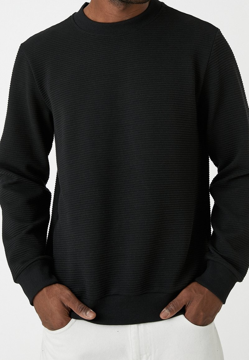 Sweat-shirt noir avec texture côtelée, encolure ronde et manches longues. Doté d'un ourlet et de poignets ajustés, réalisé dans un tissu doux.
