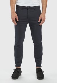 Navy slim-fit pants made from textured fabric, featuring a zipper at the ankle and a buttoned front closure with belt loops.