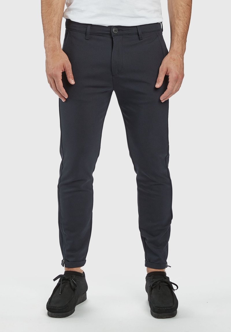 Navy slim-fit pants made from textured fabric, featuring a zipper at the ankle and a buttoned front closure with belt loops.