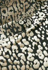 Tkanina s leopardím potiskem a plyšovou texturou v béžové a černé barvě, s různými tvary a řaseným švem podél okraje.