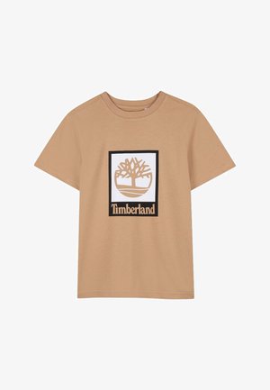 Tankleurig T-shirt met korte mouwen en een ronde hals, met een wit vierkant in het midden waarin een gestileerd boomlogo en de tekst "Timberland" eronder staan.