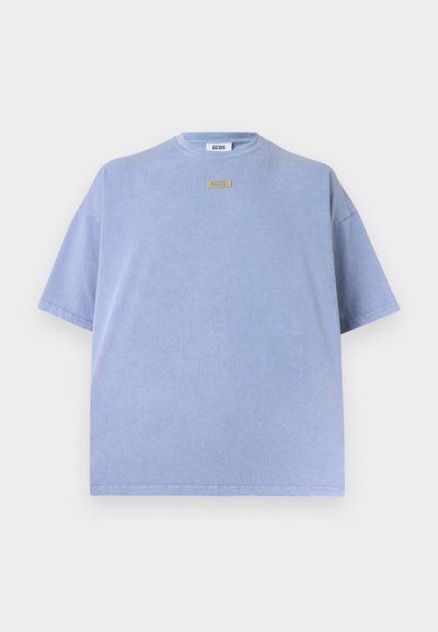 Ανοιχτό μπλε υπερμεγέθη κοντομάνικο T-shirt με στρογγυλή λαιμόκοψη και μικρή καφέ ετικέτα με την επιγραφή "GCDS" κάτω από τη λαιμόκοψη.