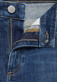 Vaqueros de mezclilla azul oscuro con un zipper plateado, costuras amarillas y un botón metálico. Presenta un bolsillo forrado y una cinturilla asimétrica.
