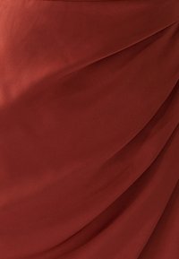 Rostfärgat tyg med en mjuk, lätt glansig textur. Draperad design skapar mjuka veck och vågor över ytan.