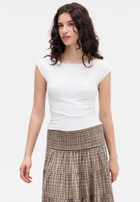 Haut ajusté blanc à manches courtes associé à une jupe à volants à carreaux beiges et bruns, avec une taille élastique et un tissu texturé.