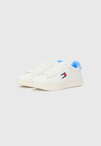 Hvite sneakers med en glatt læroverdel, lyseblå detaljer på kragen, og en logopatch med røde og blå striper på siden.