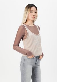 Béžová tílko s texturovaným designem přes hnědou košili s dlouhým rukávem, spárované s světle šedými skinny jeans.