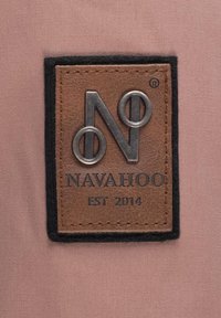 Smeđi kožni tag s urezanim logotipom "NAVAHOO" i "EST 2014", obrubljen crnom tkaninom, postavljen na svijetloružičastu pozadinu.