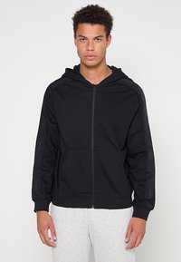 Czarna bluza z kapturem zapinana na zamek z przednią kieszenią. Posiada kaptur ze sznurkiem do regulacji oraz teksturowaną tkaninę. Ozdobiona brandingiem wzdłuż rękawów.