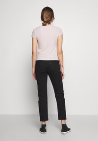 Top a maniche corte rosa chiaro a coste abbinato a jeans neri a taglio aderente. L'outfit presenta un design semplice e una texture liscia.