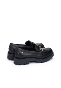 Mocasines de cuero negro con suela gruesa, que presentan un detalle de hebilla en tono dorado y acentos cosidos, textura suave y punta redonda.