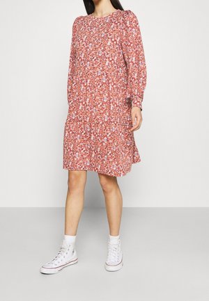 Vestido floral en color coral, con mangas largas y un corte relajado. Combinado con zapatillas altas blancas, mostrando un look divertido y casual.