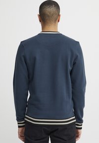 Marineblauwe sweatshirt met lange mouwen, geribbelde manchetten en een gestreepte zoom. Gladde textuur met een ronde hals en een subtiele achterkant met schoudernaad.