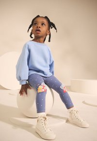 Sweat-shirt bleu clair avec manches ballon, leggings bleus à motifs ornés d'appliqués fantaisistes, et baskets blanches montantes.