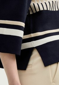 T-shirt en tricot marine avec des rayures crème horizontales et un motif texturé. Conçu avec des manches à longueur de coude et un ourlet fendu.
