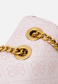 Vaaleanpunainen teksturoitu kangaskassi, jossa on kultasävytteiset metalli-aukot ja ketjuolkaimet. Kuvio on hienovarainen ja sävy sävyyn, koristeellisin yksityiskohdin.