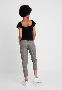 Svart kortärmad topp med samlade axlar, tillsammans med grå rutiga tapered-byxor och vita sneakers. Fokusera på avslappnade, figursydda silhuetter.